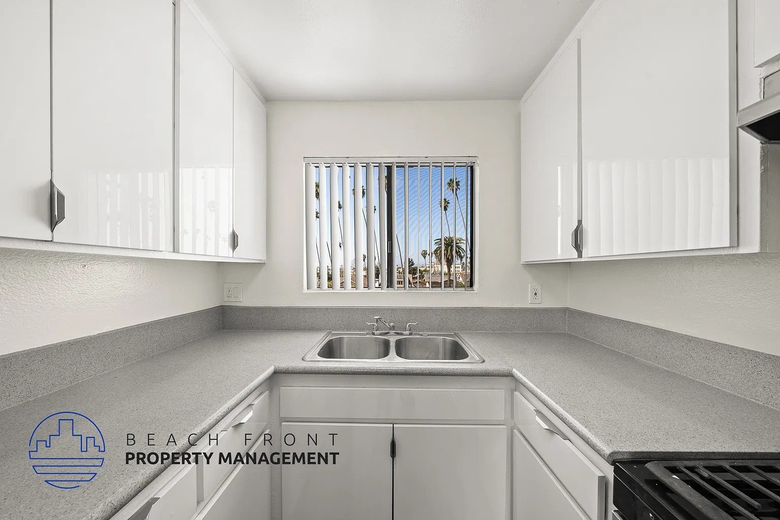 A kitchen with white cabinets and a view of the beach through the window.